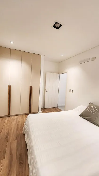 Dormitorio moderno con cama blanca, placares integrados y piso de madera — proyecto Canning, por Eniraestudio, en Canning